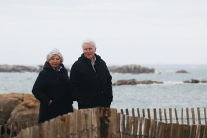 Elderly couple stands together near the ocean, enjoying a peaceful outing.
