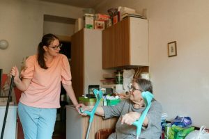 A caregiver engaging with a senior using crutches in a cozy Prague home environment.