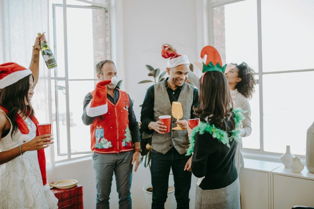 Colleagues celebrating a festive holiday party in an office setting, enjoying drinks and wearing fun costumes.