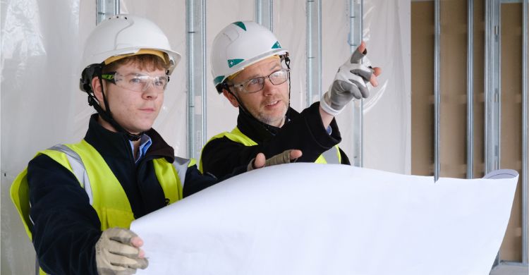 Image shows two people wearing hard hats and safety goggles looking at a large map