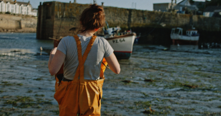 A woman in fishing gear walking towards the sea with a bucket