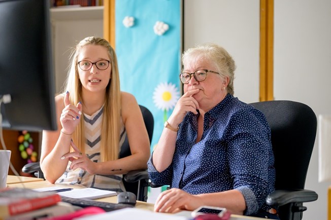 A younger woman and slightly older woman sat talking and looking at a computer