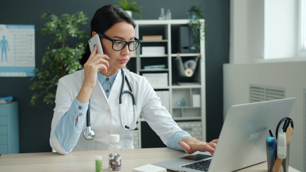 Doctor on phone, working on laptop in office.