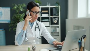 Doctor on phone, working on laptop in office.