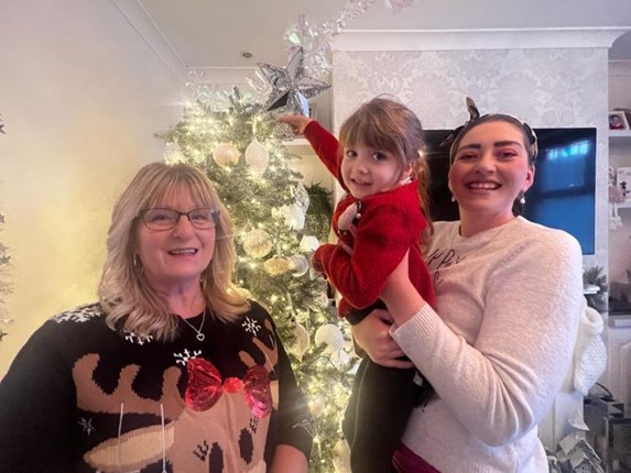 a small child is held up to put a star on a tree with her mum and shared lives carer