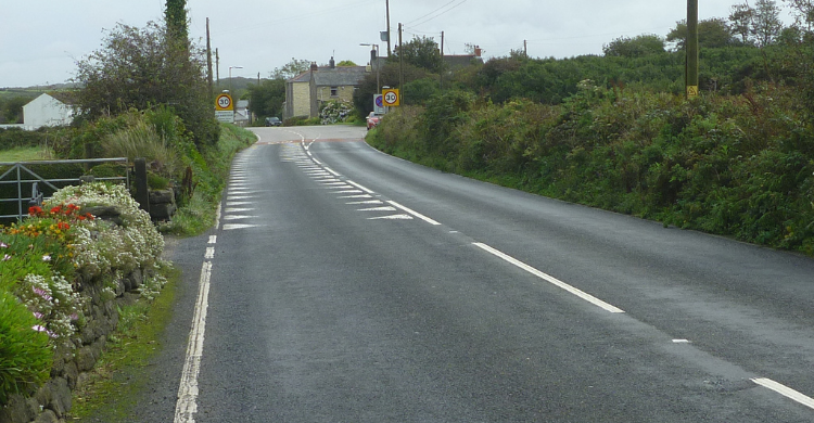 Photo shows a country road with hedging either side leading to a village with