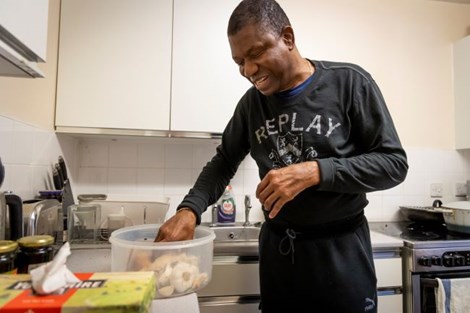 A man smiles standing in a kitchen taking cakes out of a plastic container