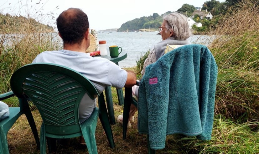 Two people, Justin and Jane are sat with their backs to the camera looking across to the sea