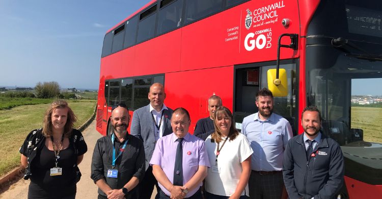 Photograph shows a group of eight people stood in front of a red double decker bus