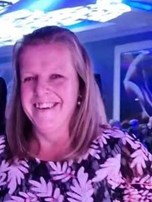 Gemma is smiling at the camera. Her hair is pulled back from her face and is shoulder length. She is wearing a blue patterned top.