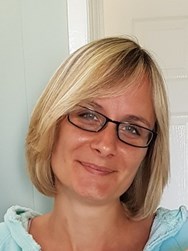 Victoria has a short blonde bob hairstyle. She is wearing glasses and smiling at the camera