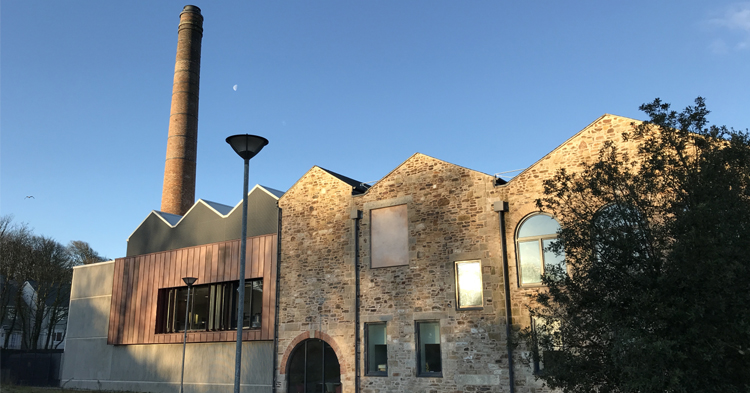 Photograph of the Kresen Kernow Cornish Studies building with it's historic chimney stack taken against a blue sunny sky
