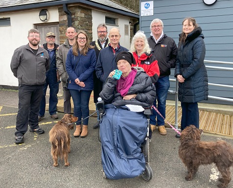 A photo of various people who attended the opening of a new Changing Places toilet in south east Cornwall. There are ten people standing in front of the building with a person in a wheelchair at the front, holding a dog on a lead