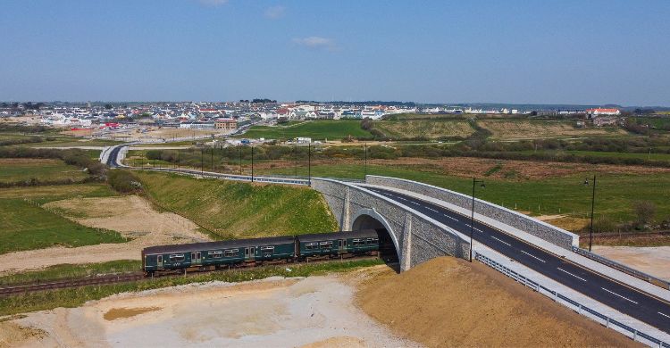 Image shows a train travelling under a new road bridge