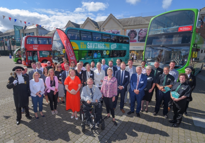 Large group of people stood in front of three double decker buses