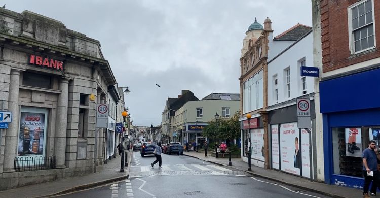 Image shows a high street with a person crossing the road and shops lining either side