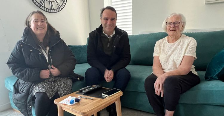 The image shows three people sat on a sofa in a new home