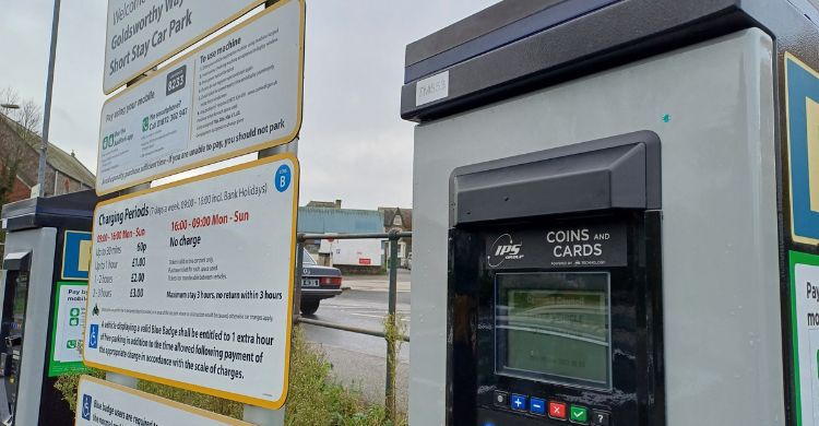 Image shows a car park ticket machine with a sign in the background